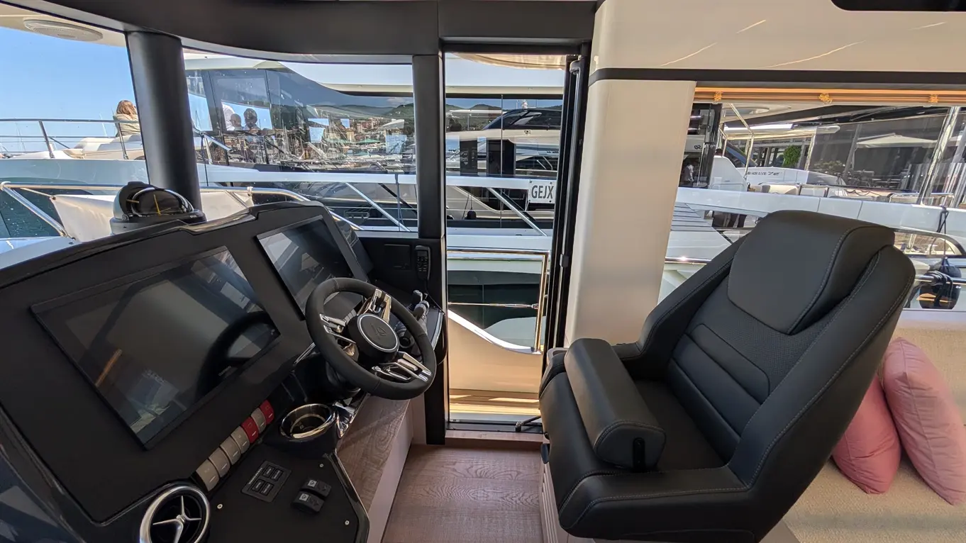 Luxury yacht interior showing a sleek helm with two screens and a black leather captain's chair, overlooking the marina.